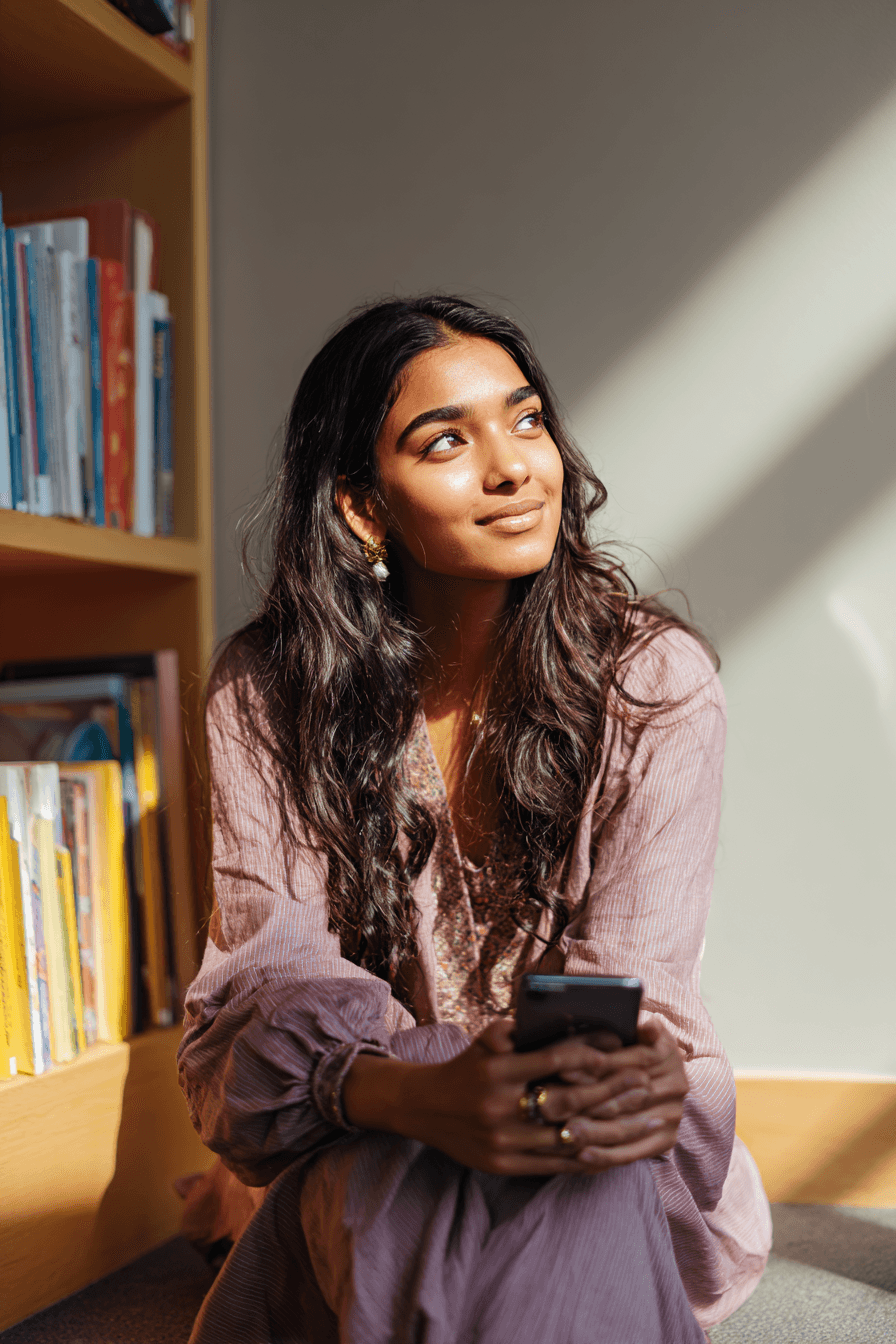 A young woman looking up from her phone with a dreamy, grateful smile